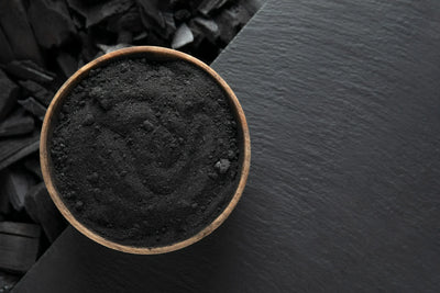 Pote com carvão em pó e ao lado pedaços de carvão representando o carvão ativado.