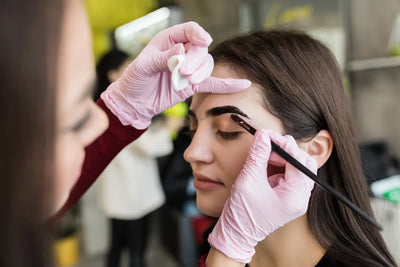 Mulher fazendo as sobrancelhas da cliente após realizar um curso de design de sobrancelhas